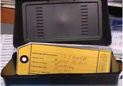 Yellow paper tags with handwritten labels in a dark container, possibly for inventory or project tracking.
